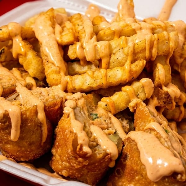 Crispy fries and fried dumplings drizzled with a creamy orange sauce in a white takeout container.