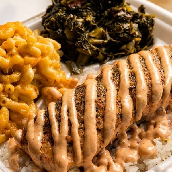 Takeout container with salmon over rice, mac and cheese, and collard greens.